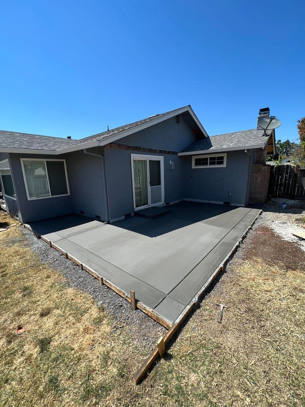 Newly poured concrete patio beside a gray house under clear blue sky.