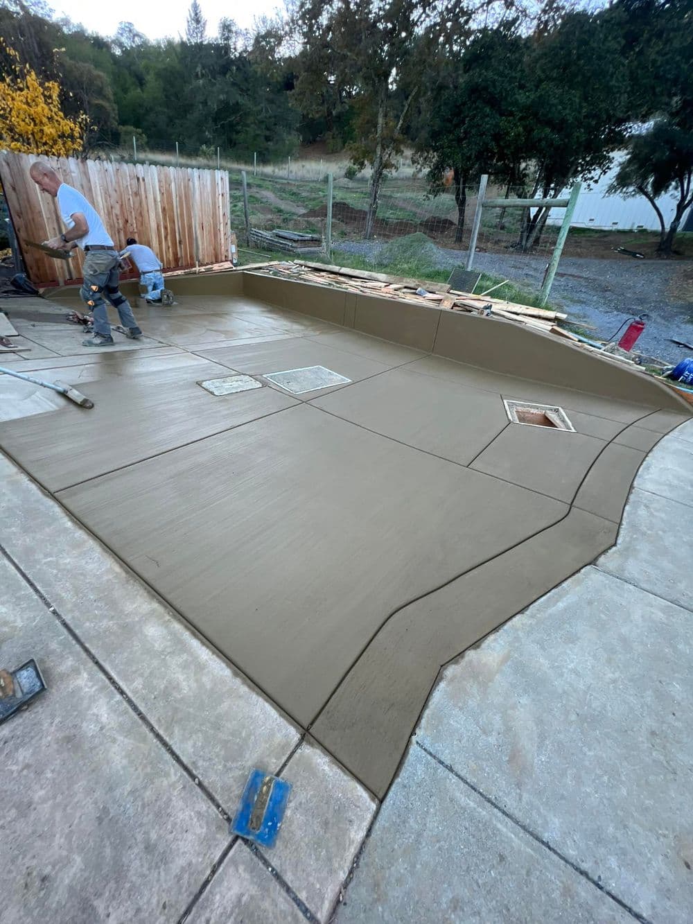 Workers applying smooth concrete finish to a newly poured pool deck in a construction site.