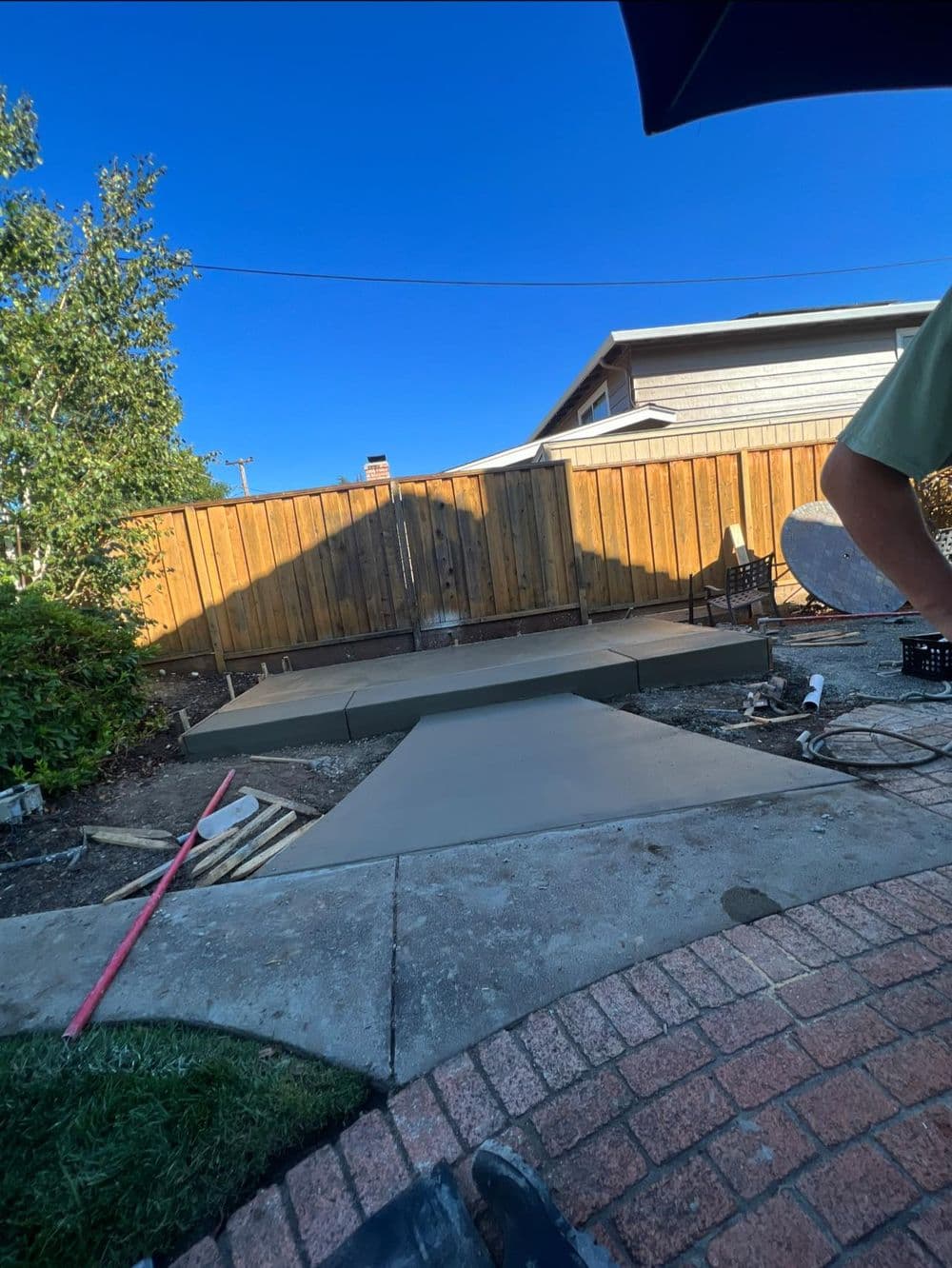 Newly poured concrete patio in backyard with wooden fence and landscaping elements.