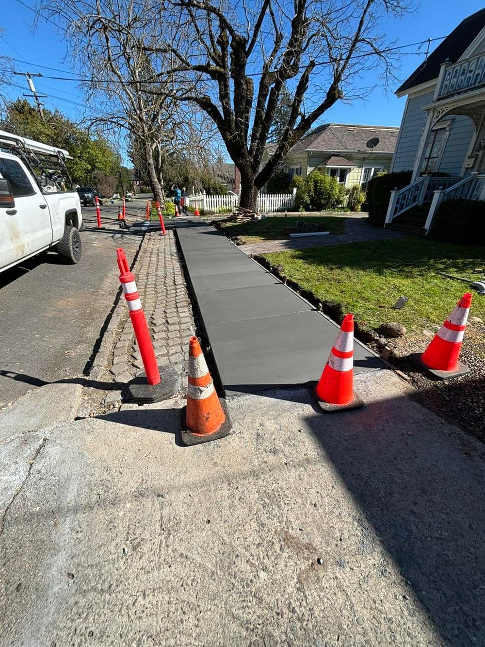 Newly poured concrete sidewalk under construction with traffic cones and a clear blue sky.