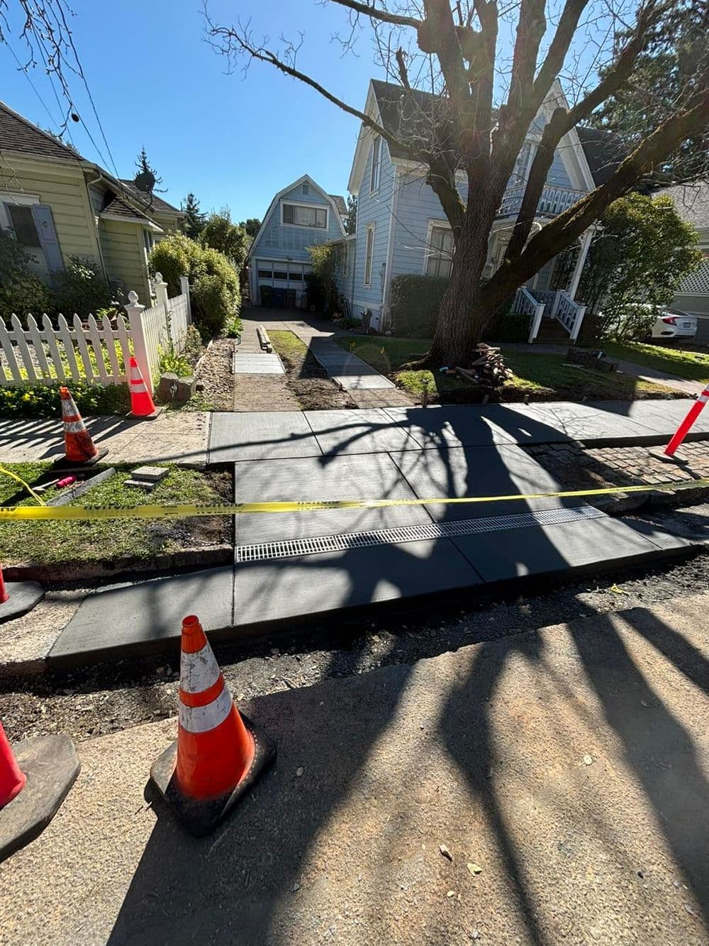 Concrete sidewalk installation with traffic cones and nearby houses in a residential area.